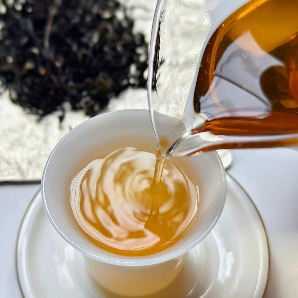 Youyun Tieguanyin Oolong Tea. Enjoying Oolong tea. Pouring a golden tea from a glass gongdao bei into a white, gongfu tea cup.