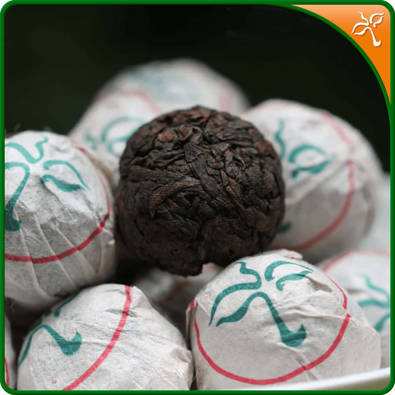 Bulang Shan Shu Puerh Dragon Pearls. Hand rolled Shu Puerh tea in a pile of paper wrapped pearls and one unwrapped.