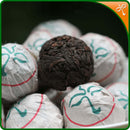 Bulang Shan Shu Puerh Dragon Pearls. Hand rolled Shu Puerh tea in a pile of paper wrapped pearls and one unwrapped.