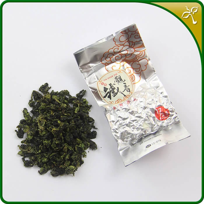 Tieguanyin oolong tea. One sealed 8g silver pouch of Tieguanyin next to some loose leaf Tieguanyin tea.